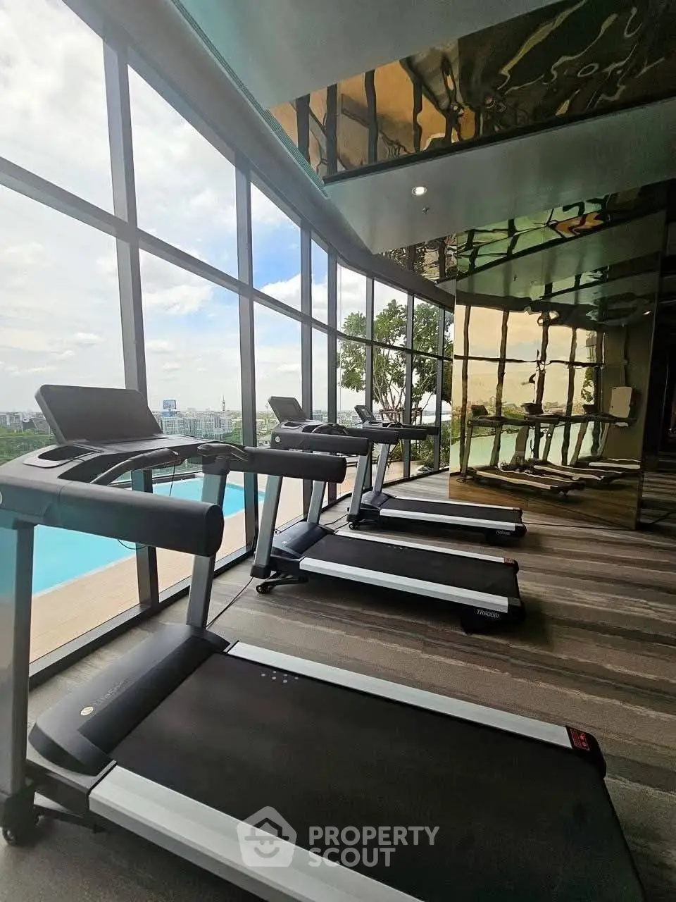 Luxurious gym with panoramic pool view and modern treadmills in high-rise building.