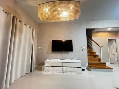 Modern living room with elegant chandelier and wall-mounted TV, featuring stylish staircase and sleek decor.