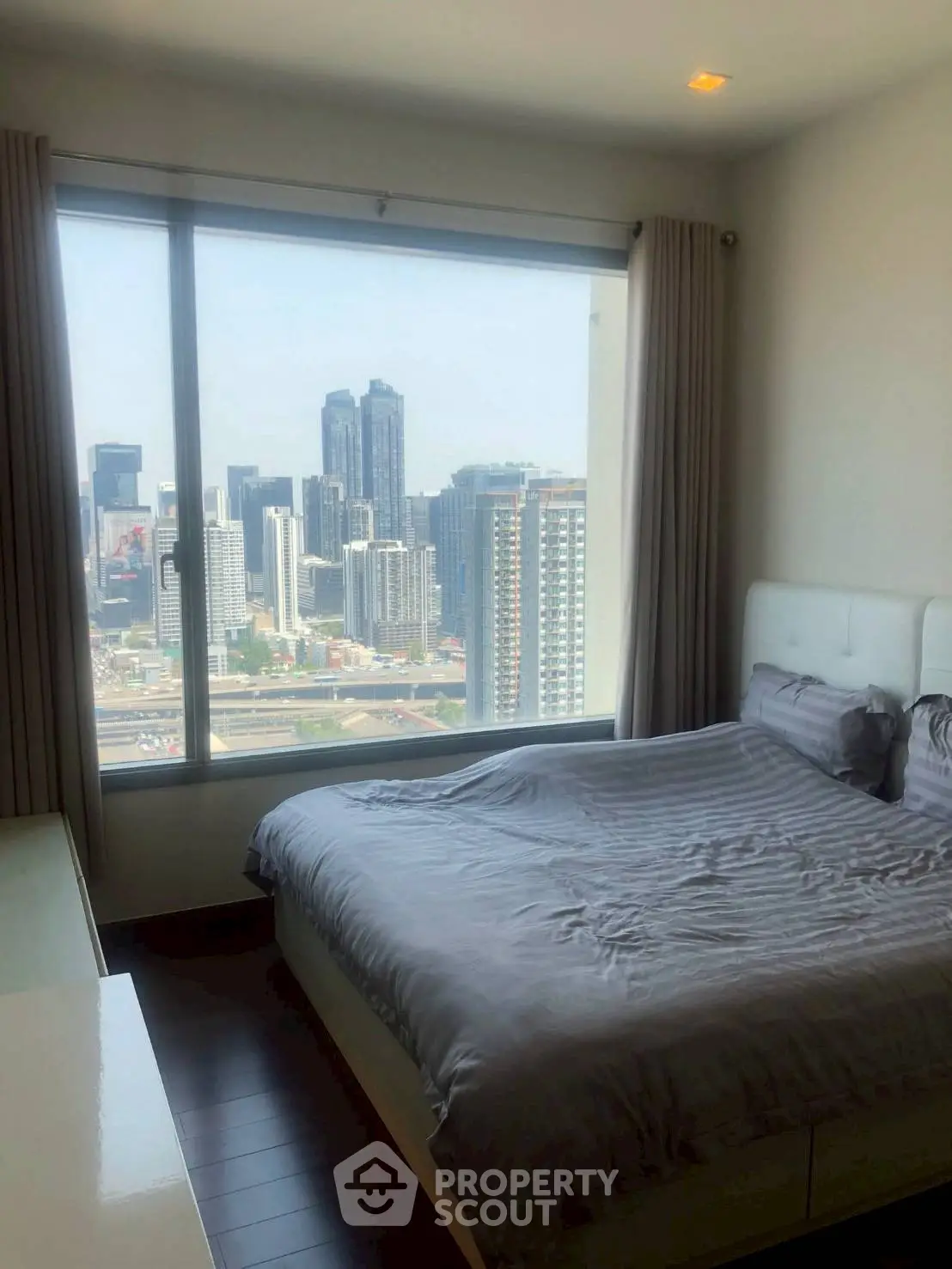 Modern bedroom with stunning city view from large window, featuring sleek furnishings and cozy ambiance.