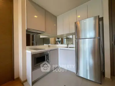 Modern kitchen with sleek cabinetry, stainless steel fridge, and built-in microwave in a compact layout.