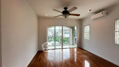 Spacious living room with wooden floors and ceiling fan, featuring large windows and sliding doors to balcony.