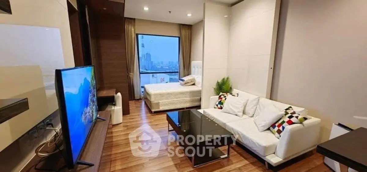 Modern studio apartment with stylish living area and city view, featuring sleek furniture and wooden flooring.