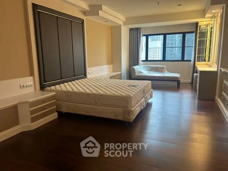 Spacious bedroom with elegant wood flooring and large window offering natural light.