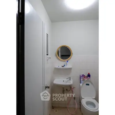 Compact bathroom with round mirror and essential fixtures, ideal for small spaces.