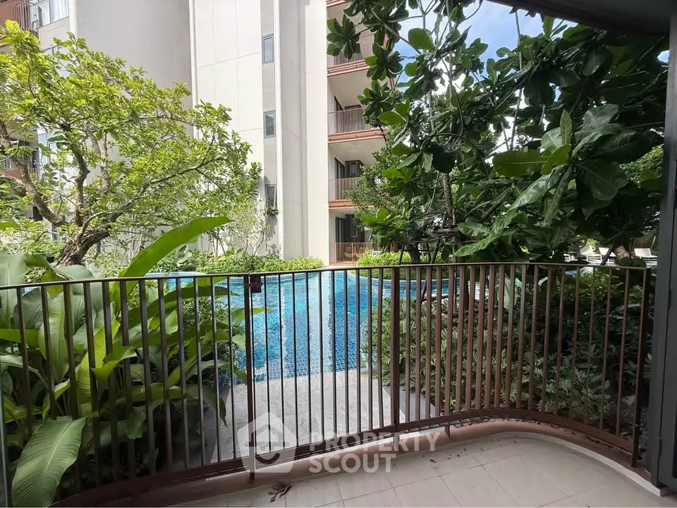 Charming balcony view overlooking lush garden and sparkling pool in modern residential complex.