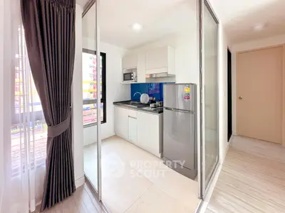Modern compact kitchen with sleek appliances and glass partition in a bright apartment.