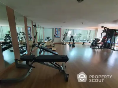 Spacious gym with modern equipment and mirrored walls in a residential building.