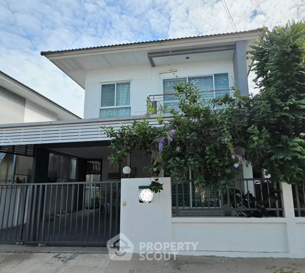 Modern two-story house with balcony and gated driveway in a suburban neighborhood.