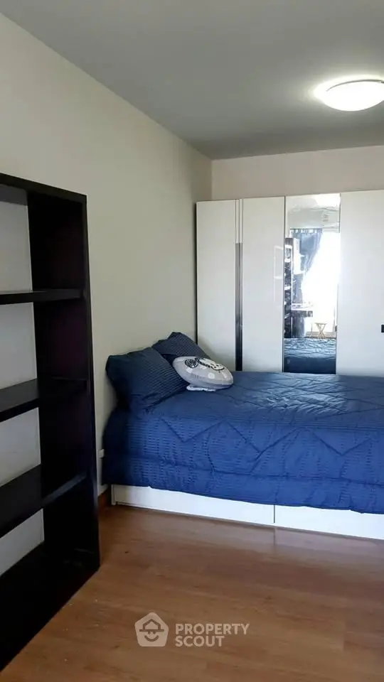 Cozy bedroom with blue bedding, mirrored wardrobe, and wooden flooring.