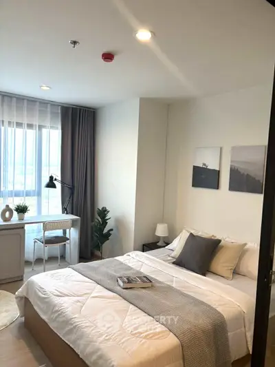 Modern bedroom with cozy decor and natural light, featuring a work desk and stylish bedding.
