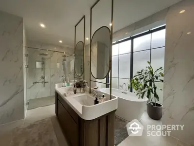 Luxurious bathroom with marble tiles, dual vanity, large mirrors, freestanding tub, glass shower, and a touch of greenery for a serene spa-like retreat.