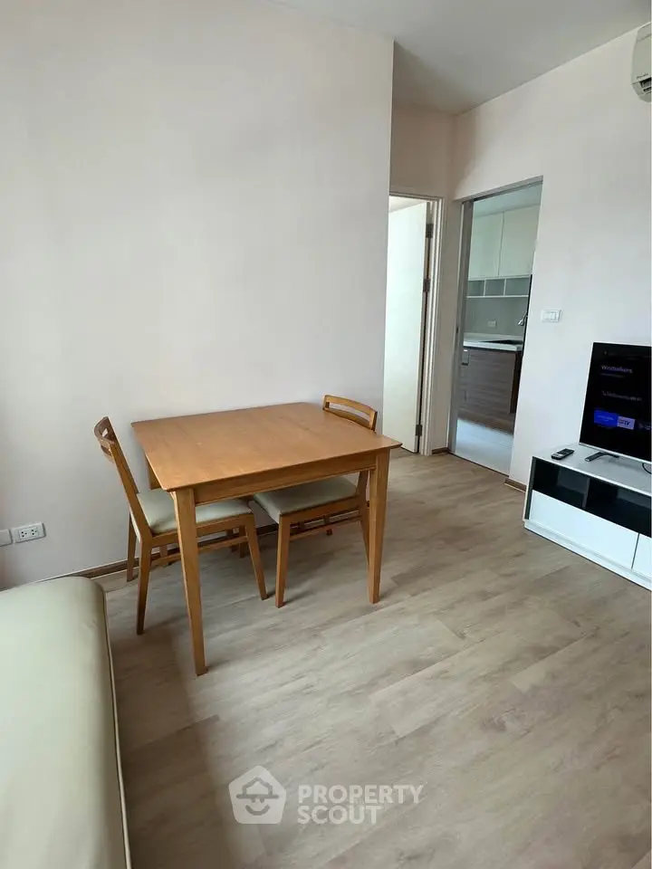 Modern living room with dining area and view into a sleek kitchen, featuring light wood flooring and minimalist design.