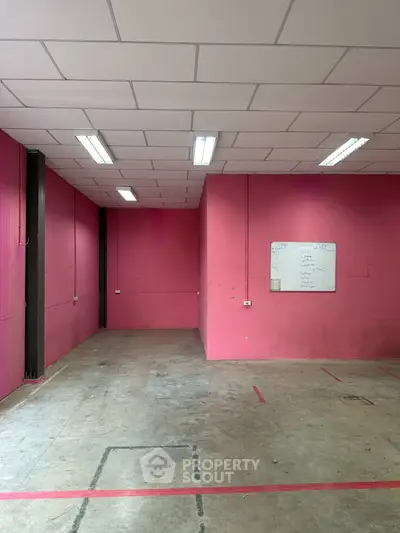 Spacious industrial-style room with vibrant pink walls and ceiling lights, ideal for creative workspace.