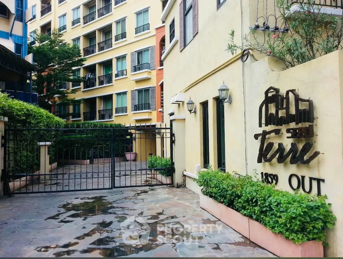 Charming residential building entrance with gated access and lush greenery.