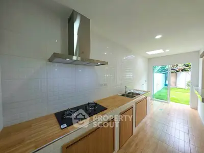 Modern kitchen with gas stove and wooden countertops, opening to a lush green garden.