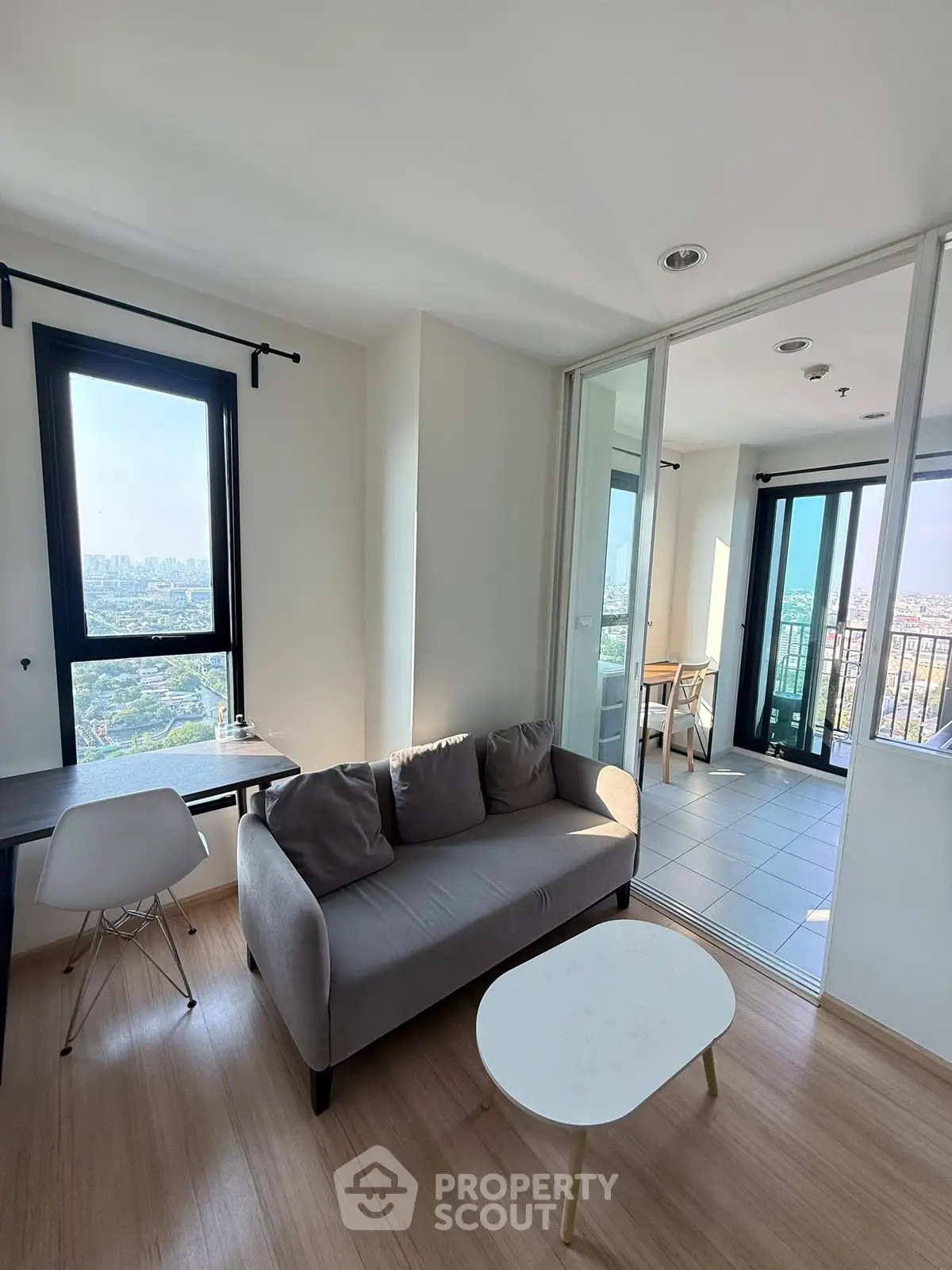 Modern living room with balcony and city view, featuring sleek furniture and abundant natural light.