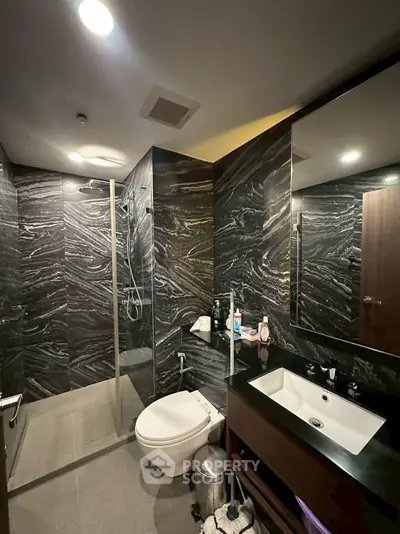 Luxurious modern bathroom with sleek black marble walls and glass shower enclosure.