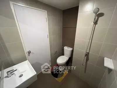 Modern bathroom with sleek fixtures and neutral tiles, featuring a shower and toilet.