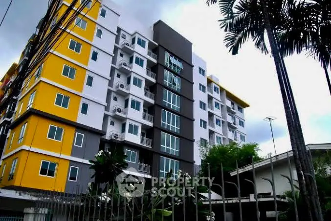 Modern multi-story apartment building with vibrant yellow accents and lush greenery.
