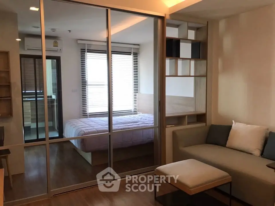 Modern apartment interior with cozy living room and stylish bedroom separated by glass sliding doors.
