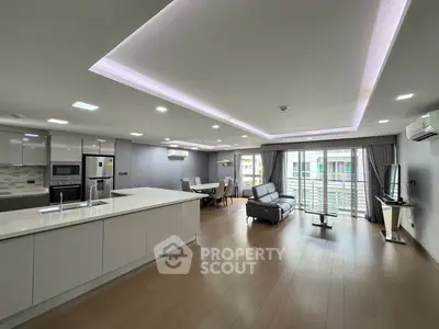 Spacious modern living room with open kitchen and balcony access, featuring sleek design and ample natural light.