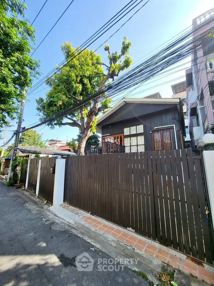 Charming residential property with wooden fence and lush tree in a quiet neighborhood.