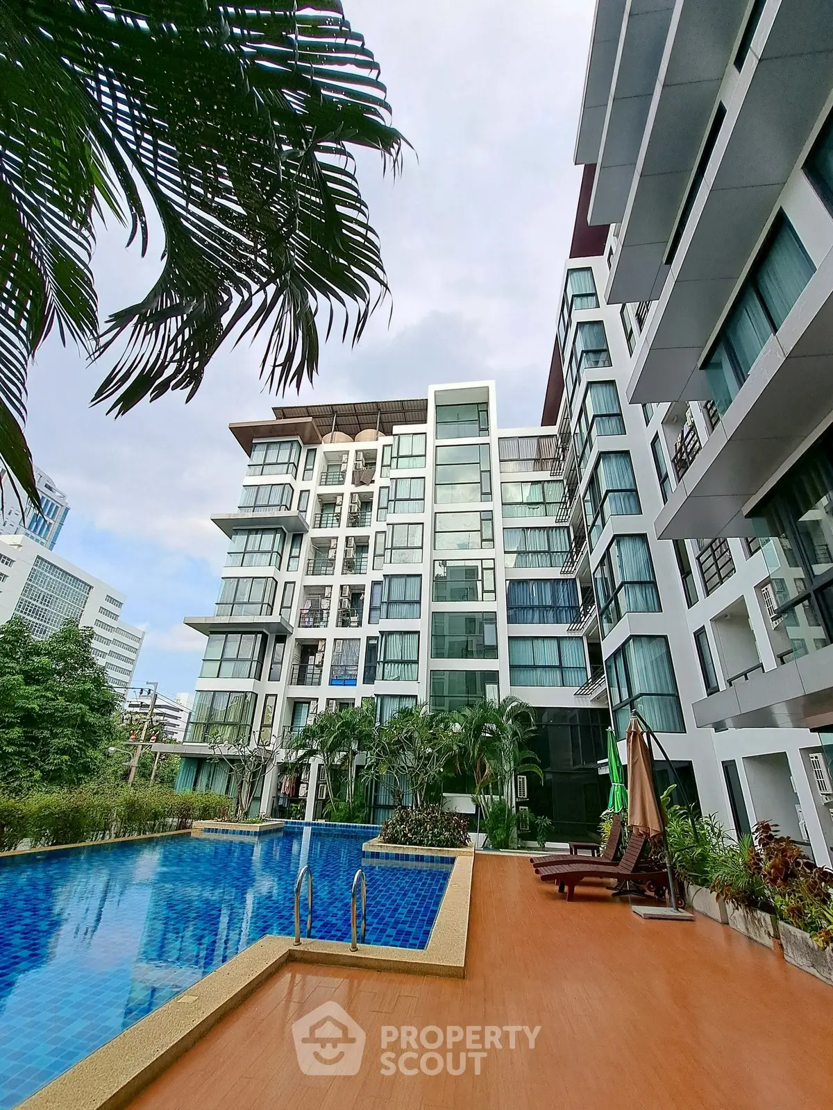 Modern apartment building with pool and lush greenery in urban setting.