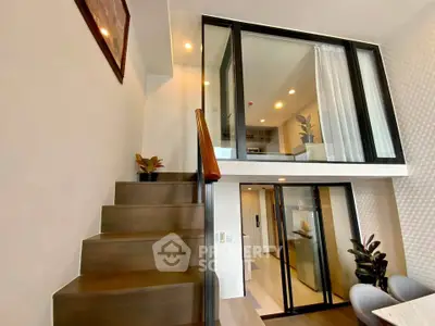 Modern duplex apartment with stylish staircase and glass-walled upper level, featuring contemporary decor and ample natural light.