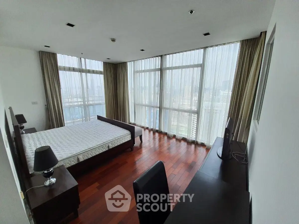 Spacious bedroom with floor-to-ceiling windows and city view, featuring hardwood floors and modern furnishings.