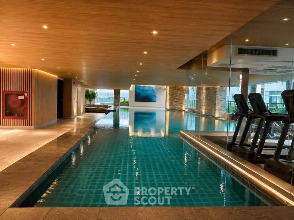 Luxurious indoor pool with modern design and gym equipment in upscale residential building.