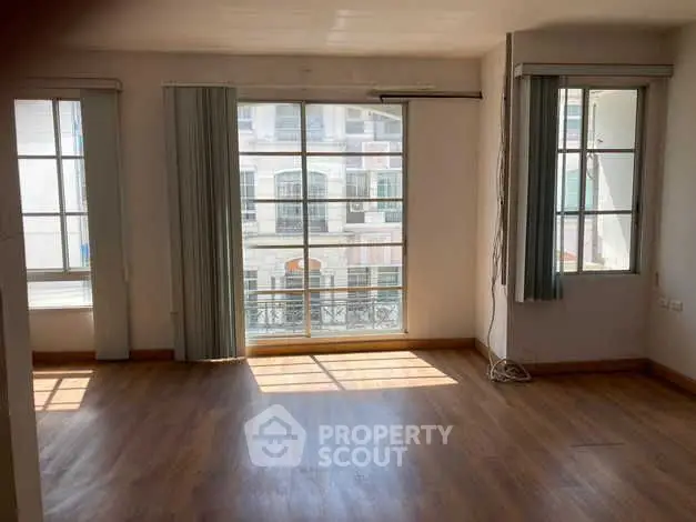 Spacious sunlit room with large windows and wooden flooring in modern apartment.