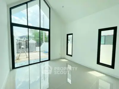 Bright modern room with high ceilings and large windows, offering ample natural light and sleek tile flooring.