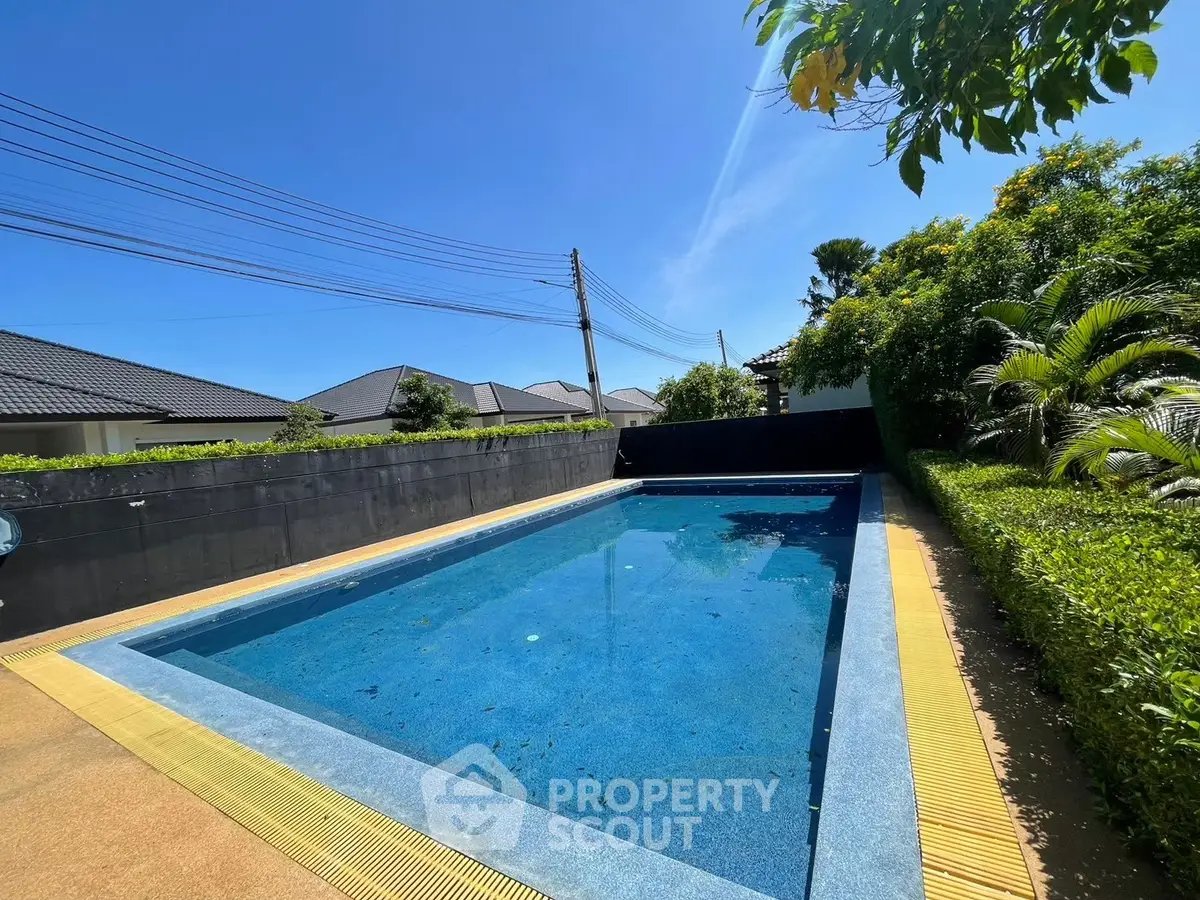 Luxurious private pool with lush greenery and clear blue sky, perfect for relaxation.