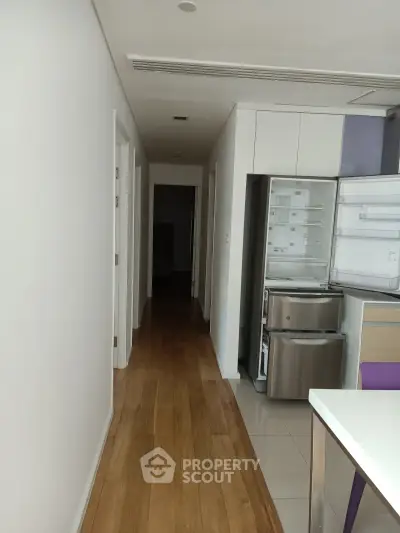 Modern kitchen with open fridge and sleek wooden flooring in a contemporary apartment.