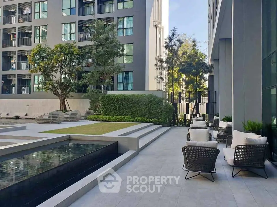 Modern apartment building with stylish outdoor seating and water feature in a serene setting.