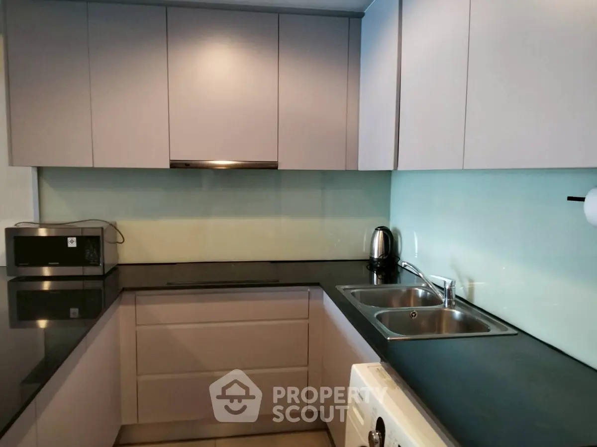 Modern kitchen with sleek cabinetry and dual sinks, featuring a washing machine and microwave.