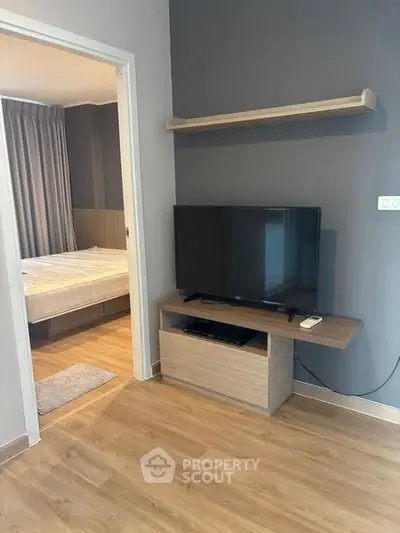 Modern living room with TV and view into cozy bedroom, featuring sleek wooden flooring.