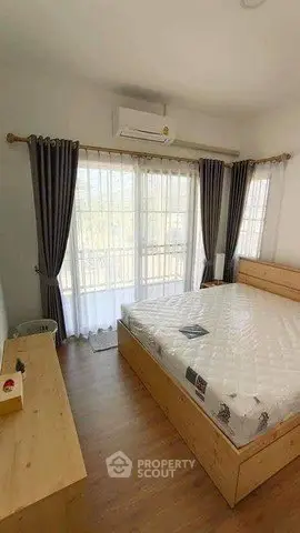 Bright bedroom with large windows and wooden furniture, featuring a comfortable bed and air conditioning.