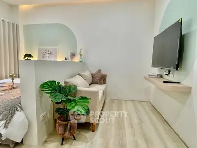 Modern living room with minimalist decor and wall-mounted TV, featuring a cozy sofa and stylish plant accents.