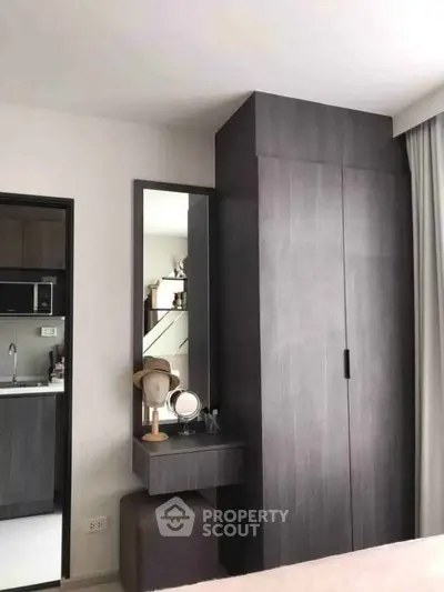 Modern bedroom with sleek wardrobe and vanity, adjacent to a compact kitchen area.