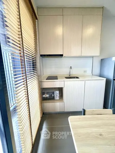 Modern kitchen with sleek cabinetry and natural light from large window blinds.