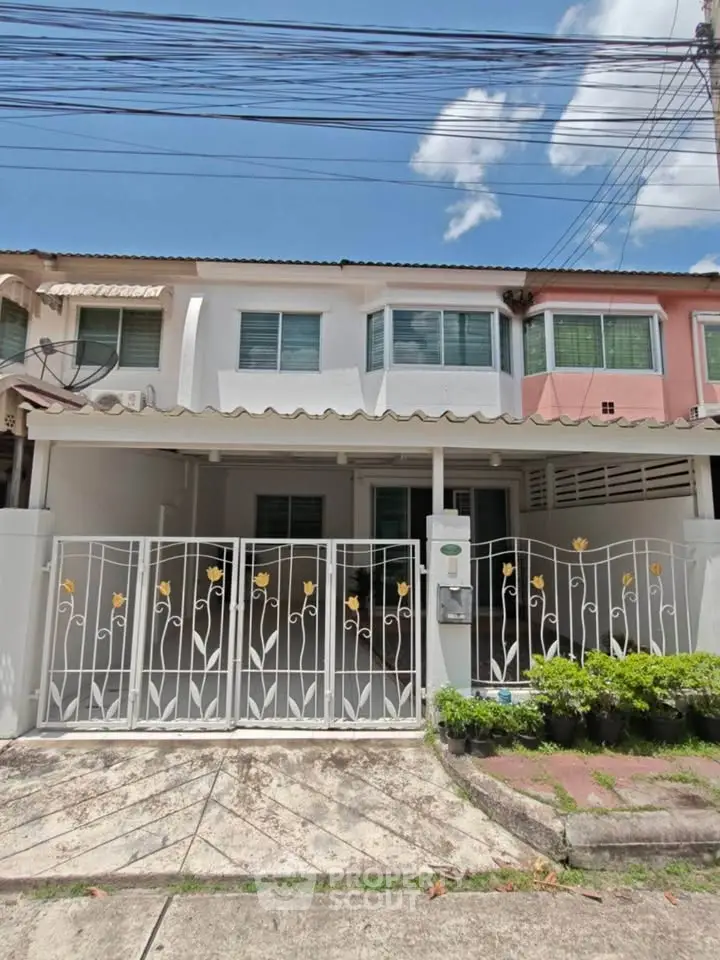 Charming townhouse with gated entrance and lush greenery under a clear blue sky.
