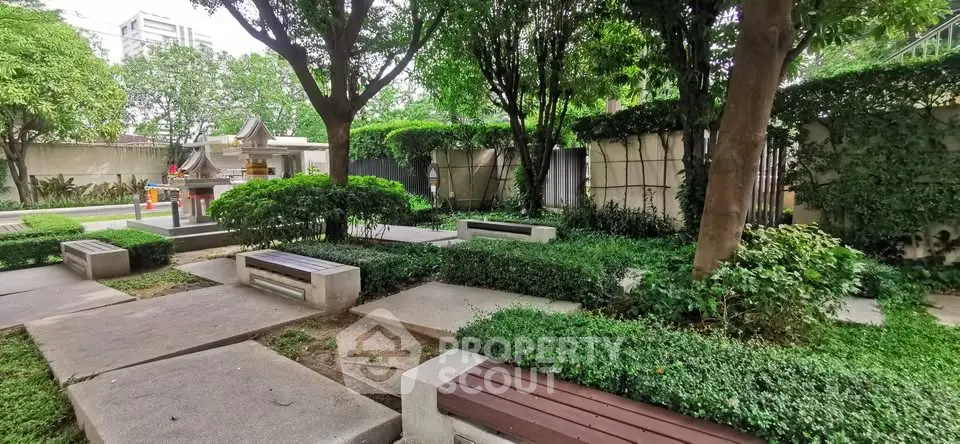 Serene garden area with lush greenery and seating in a residential complex.
