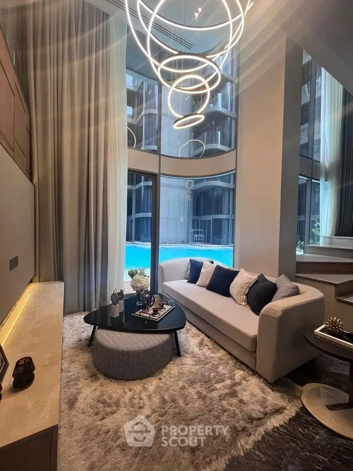 Luxurious living room with modern chandelier and pool view, featuring elegant decor and plush furnishings.