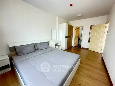 Spacious bedroom with modern furnishings and wooden flooring in a well-lit apartment.