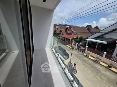 Modern balcony with glass railing offering a scenic street view in a residential neighborhood.