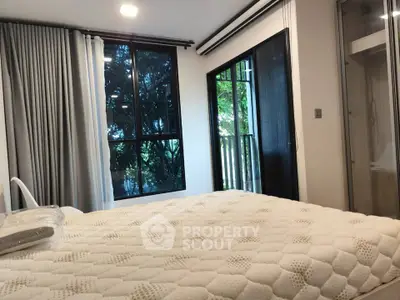 Cozy bedroom with large windows and balcony view, featuring modern decor and natural light.