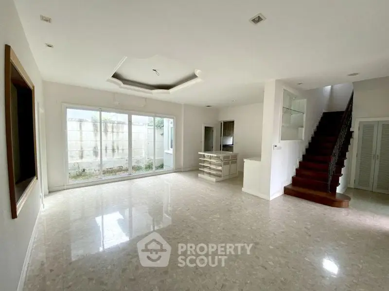 Spacious open-plan living room with large windows and elegant staircase