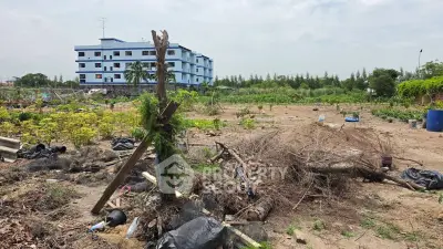 Vacant land with potential for development near a blue building, surrounded by greenery.
