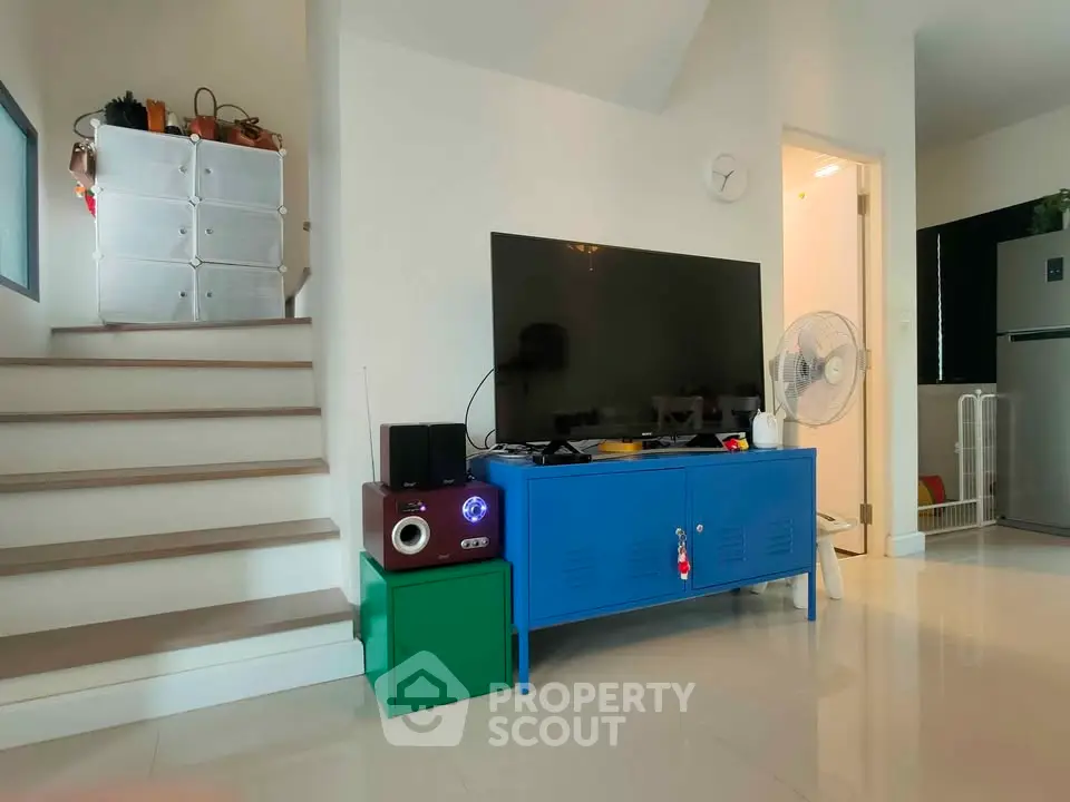 Modern living room with stylish TV setup and staircase, featuring sleek storage solutions and contemporary decor.